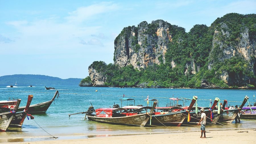 Des longtails tirés sur le sable d'Ao Nang, avec le cap calcaire au bout de la plage