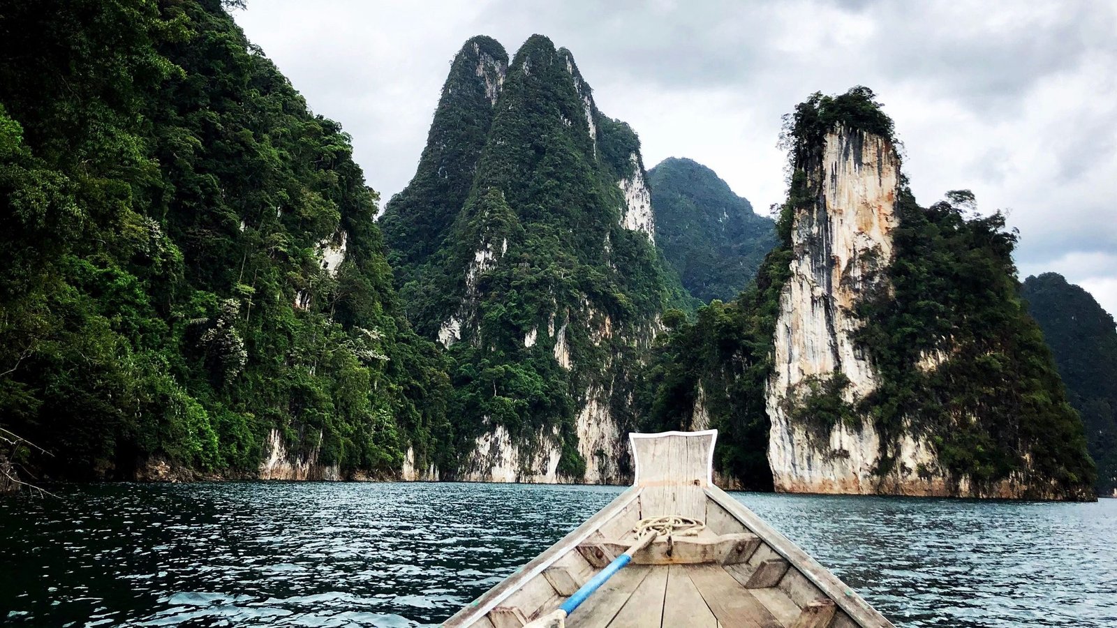 The bow of a longtail boat heading towards forested limestone stacks rising from Cheow Lan Lake