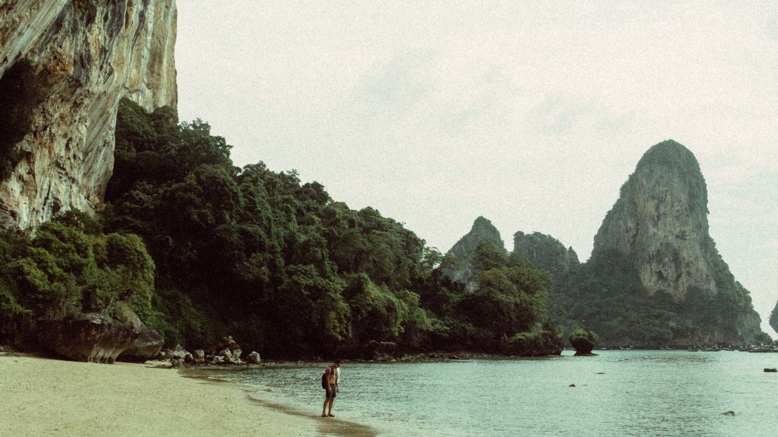 A quiet beach at the foot of a limestone cliff, with a rock pinnacle offshore