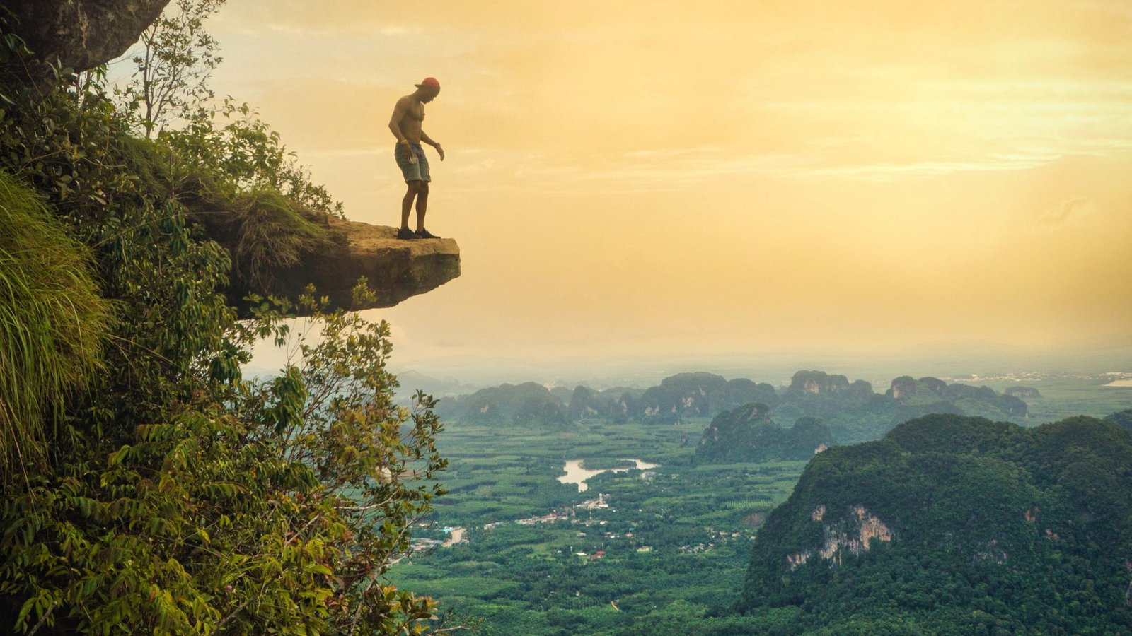 A hiker on the rock overhang at the top of Dragon Crest, above a plain of forest and limestone peaks
