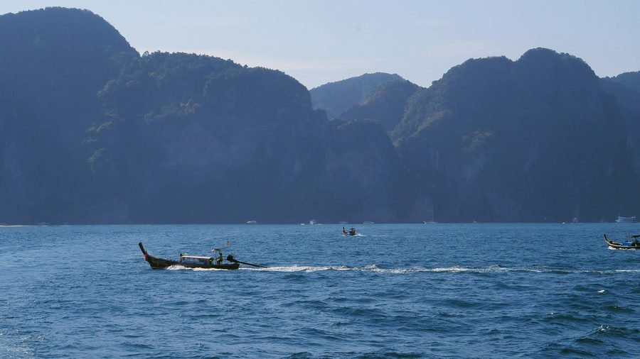 Longtail boats crossing open sea in front of tall forested limestone cliffs