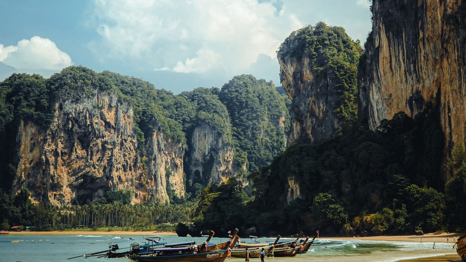 Des falaises calcaires au-dessus d'une plage de la côte de Krabi, des longtails tirés au bord de l'eau