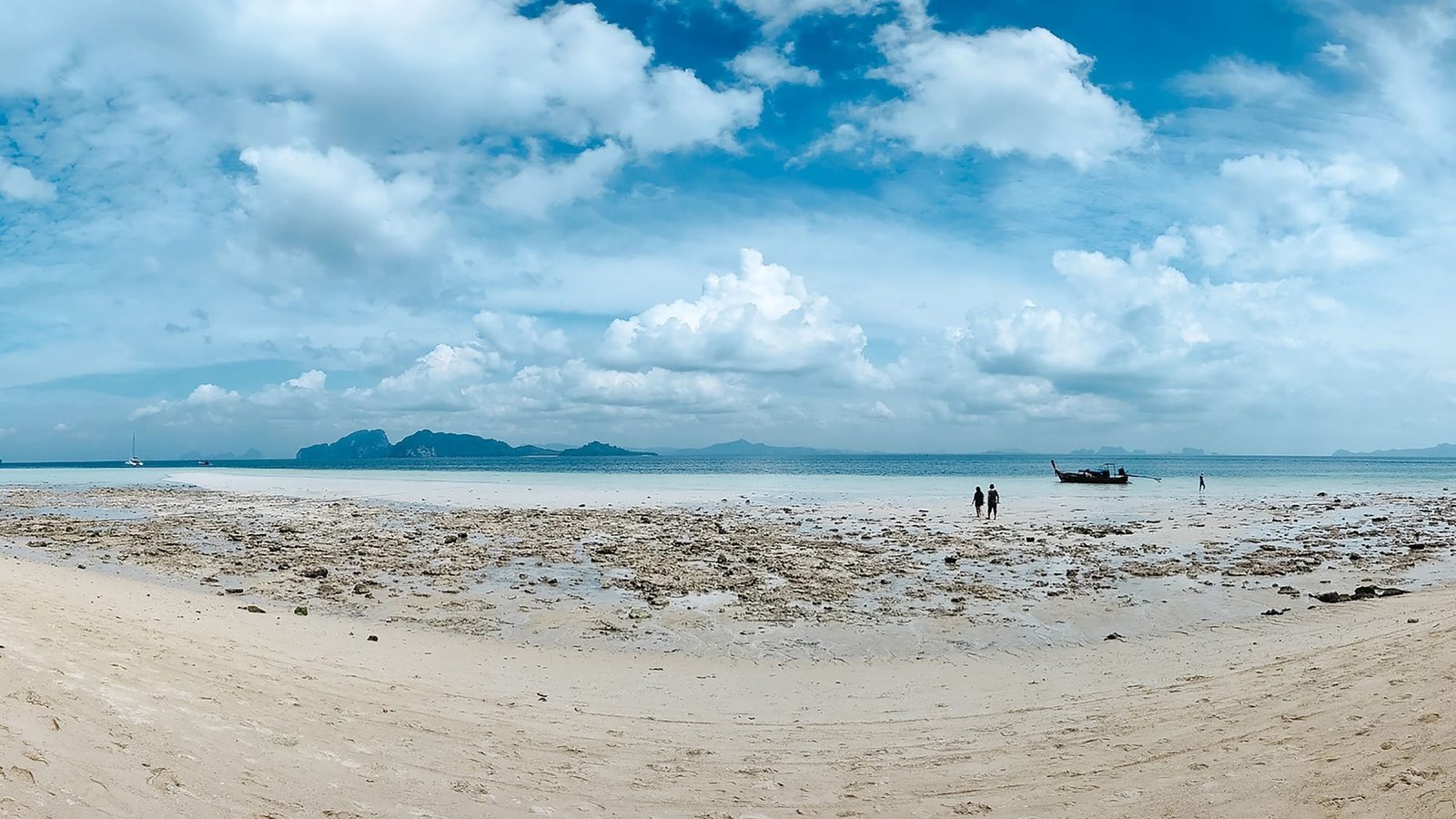 Une plage d'île tranquille à marée basse, le platier découvert et un longtail au mouillage