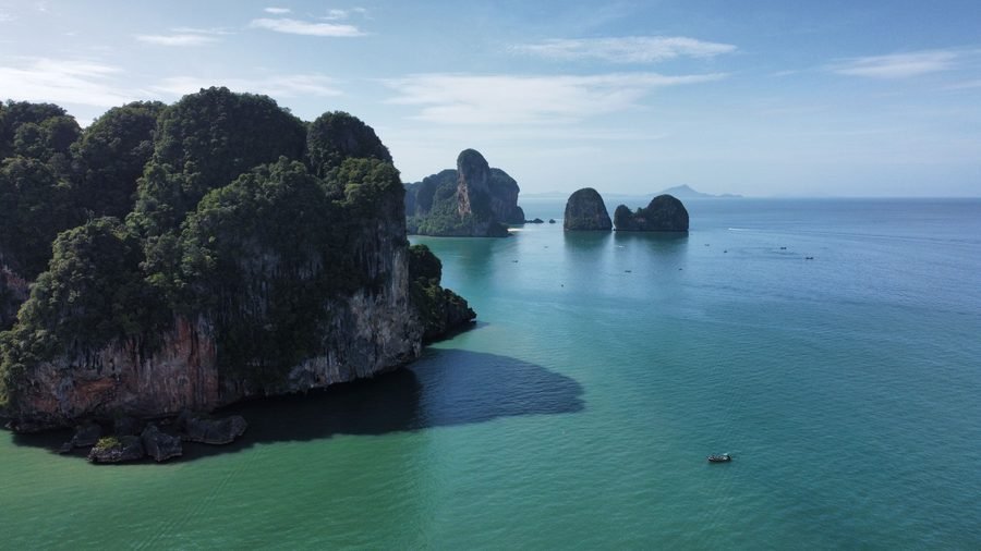 A forested limestone headland and offshore stacks rising from a calm green sea, seen from the air