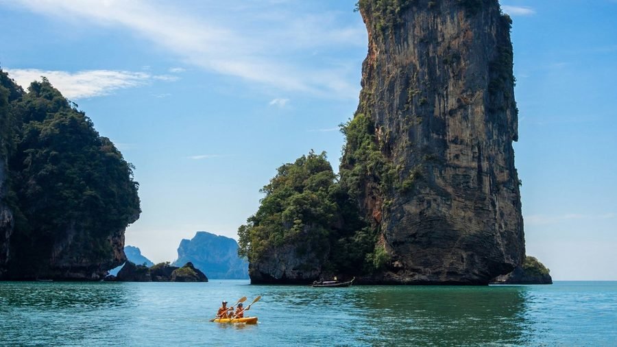 Two people in a yellow kayak paddling below a tall limestone pillar