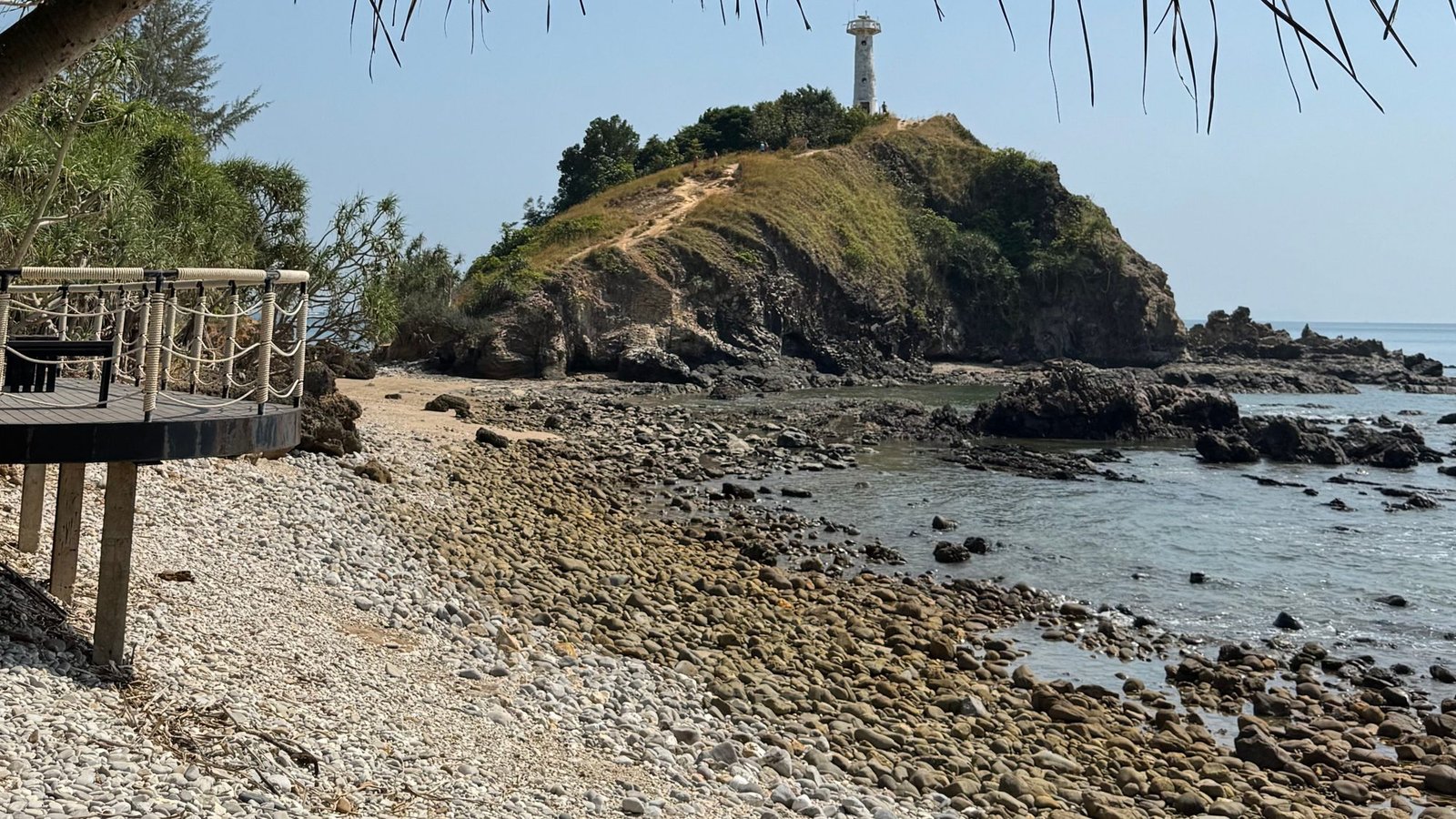The white lighthouse on the headland at the southern tip of Koh Lanta, above a pebble shore