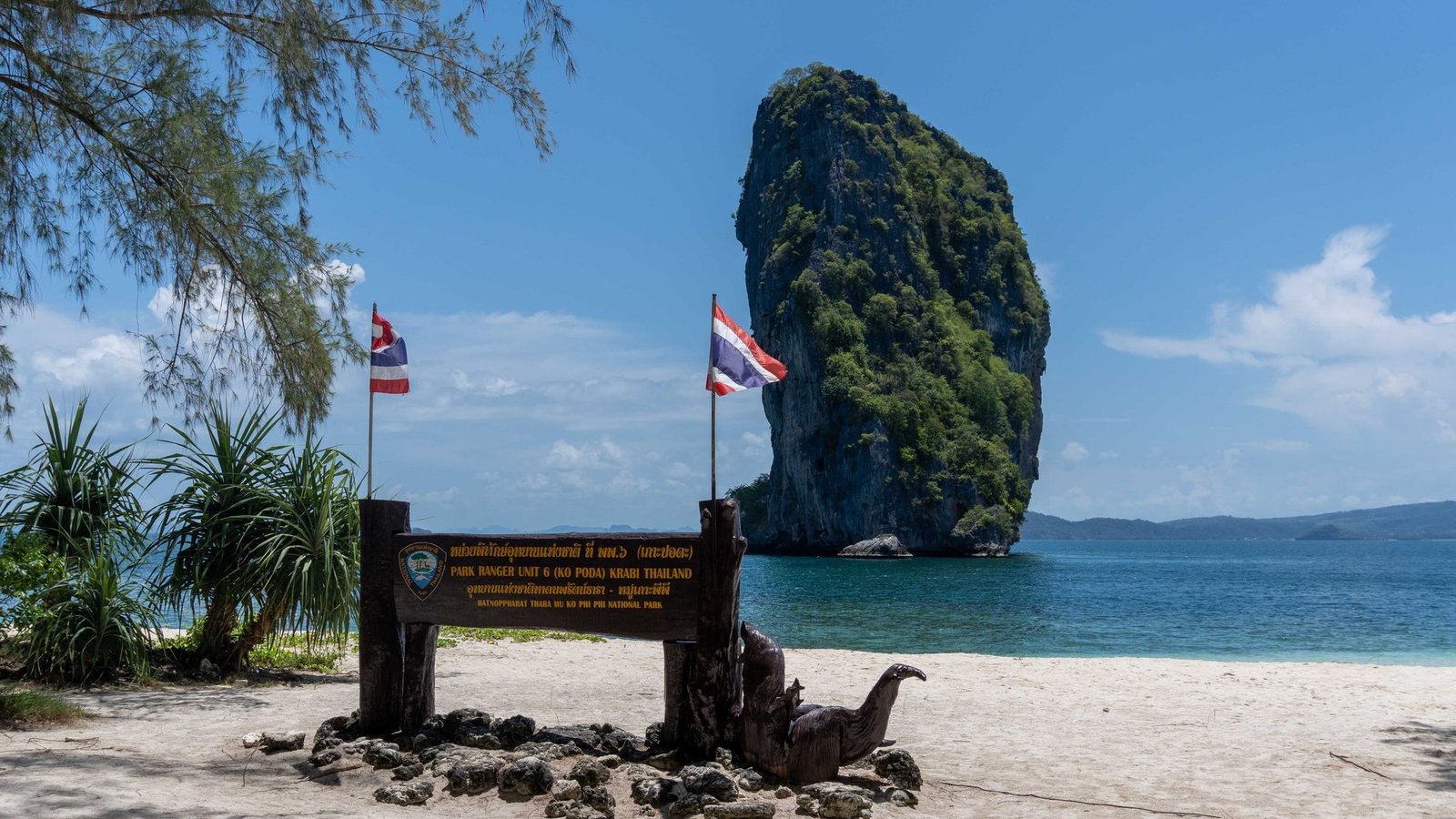 The beach of Koh Poda with the national park sign, and the island's limestone pinnacle offshore