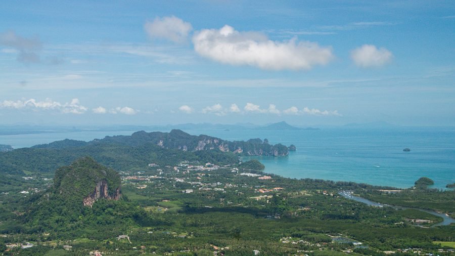 The Krabi plain seen from a hilltop, a wooded limestone peak in front and the coast and sea beyond