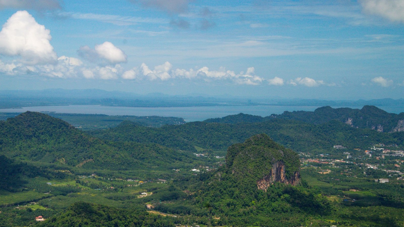 Forested hills and a limestone outcrop rolling down to the coast under a blue sky