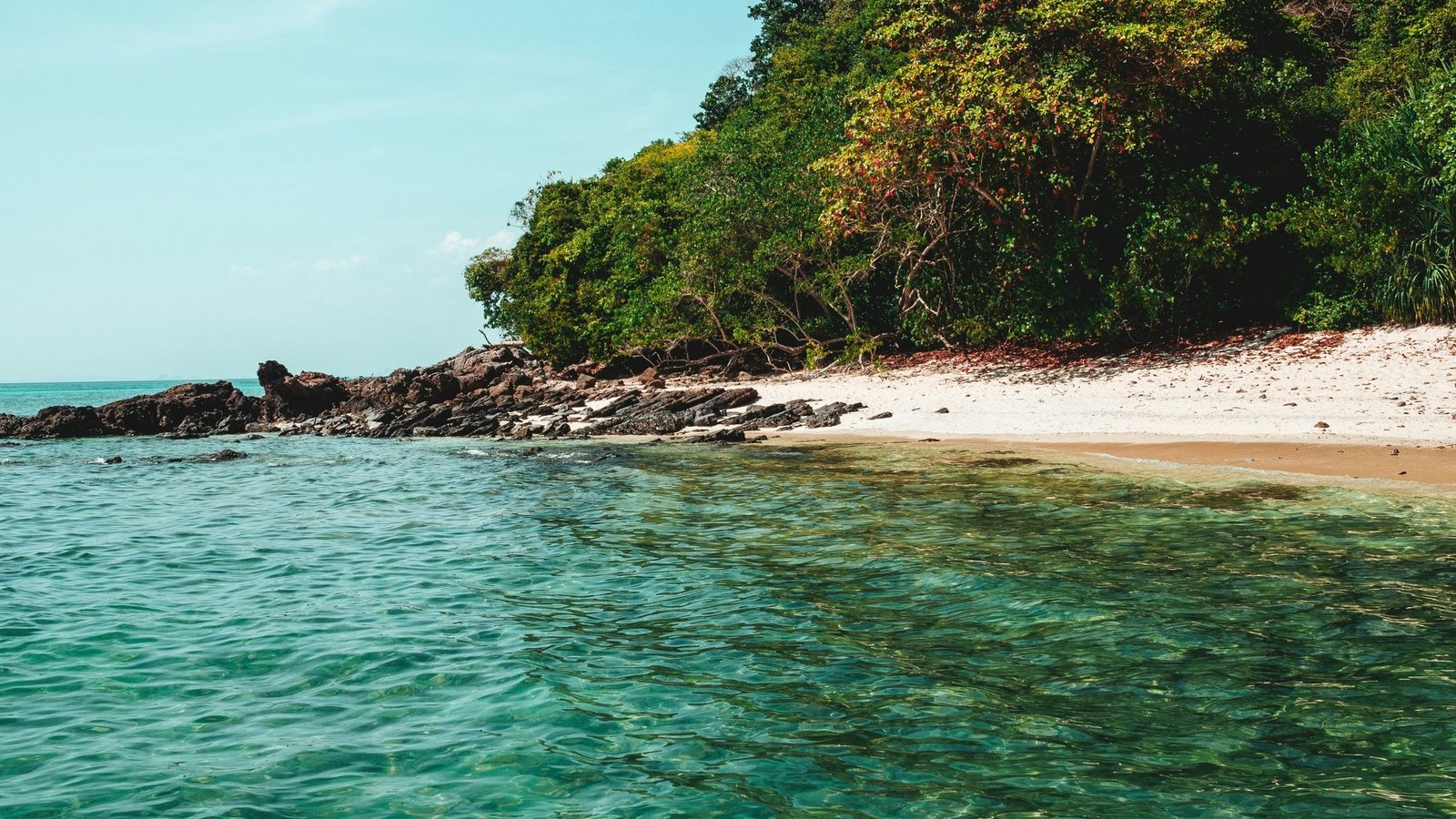 A small white sand beach below the forest on Koh Lanta, calm clear water in the foreground