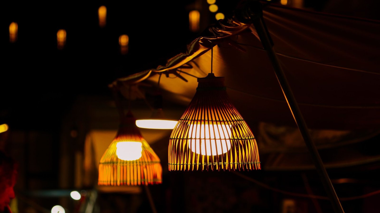 Des lampes en rotin tressé allumées au-dessus d'un étal de marché, le soir