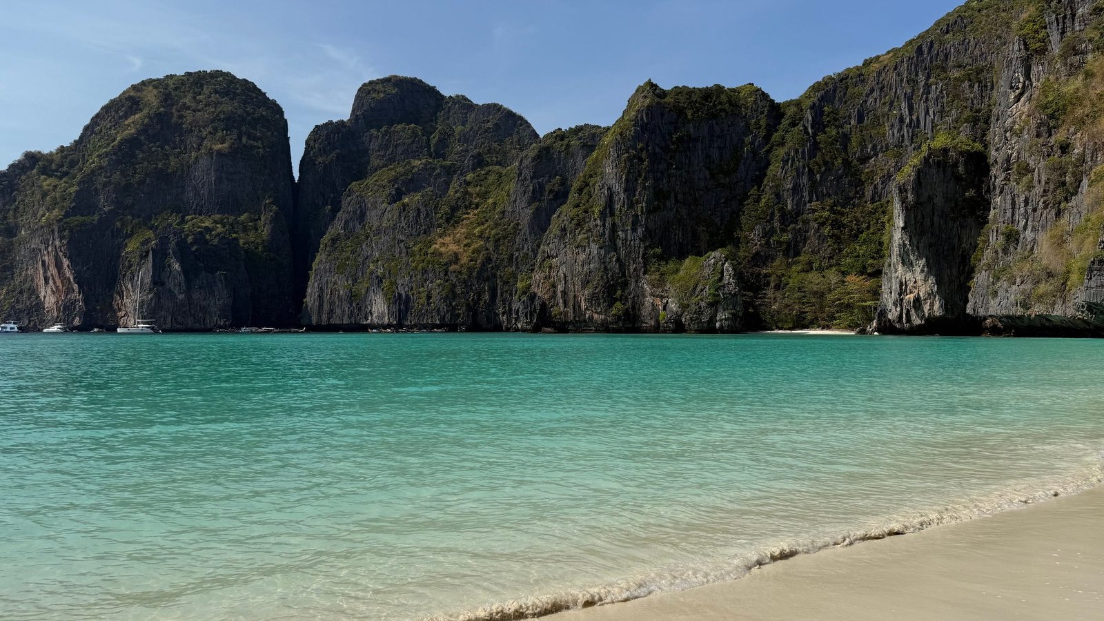 The wall of cliffs around Maya Bay above turquoise water, seen from the sand