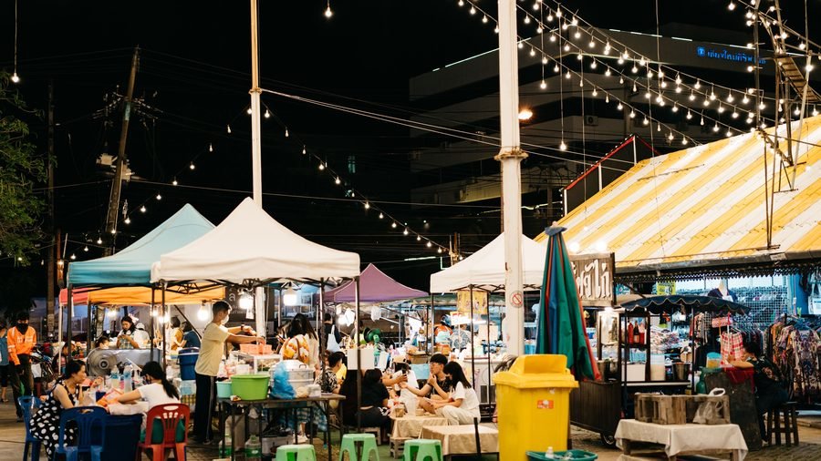 Thai night market with food stalls, string lights and plastic stools