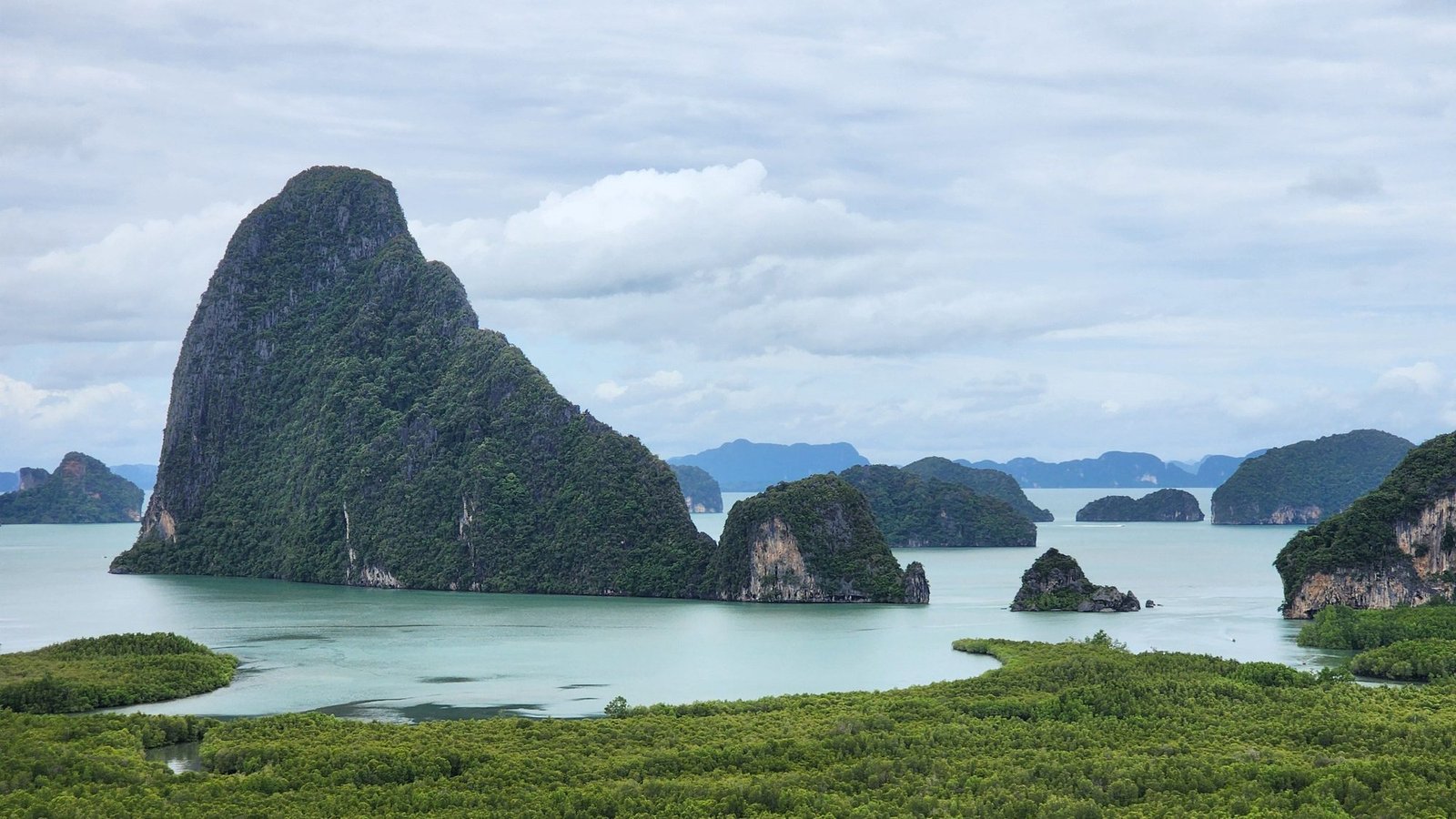 Limestone towers rising from a shallow bay above a band of mangrove forest in Phang Nga Bay