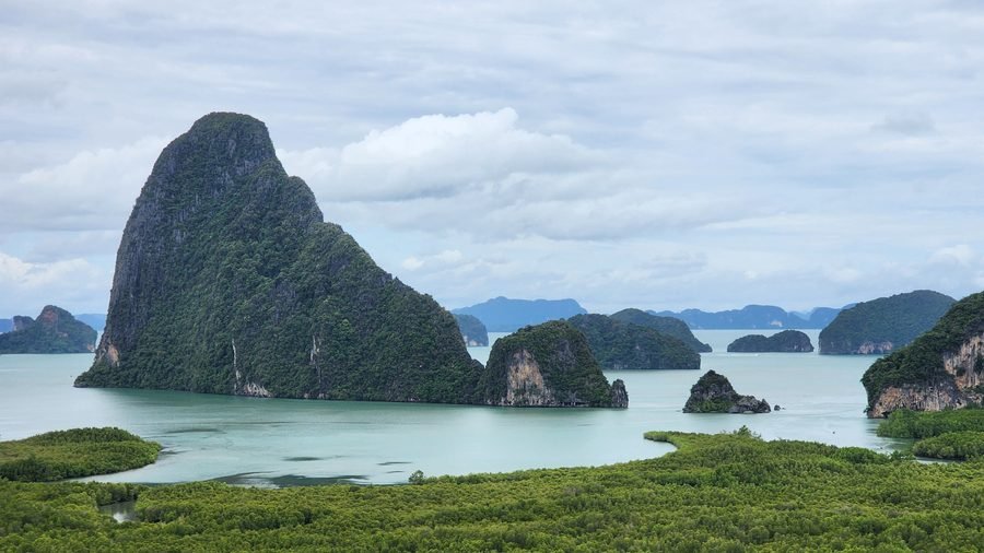 Limestone towers rising from a shallow bay above a band of mangrove forest in Phang Nga Bay