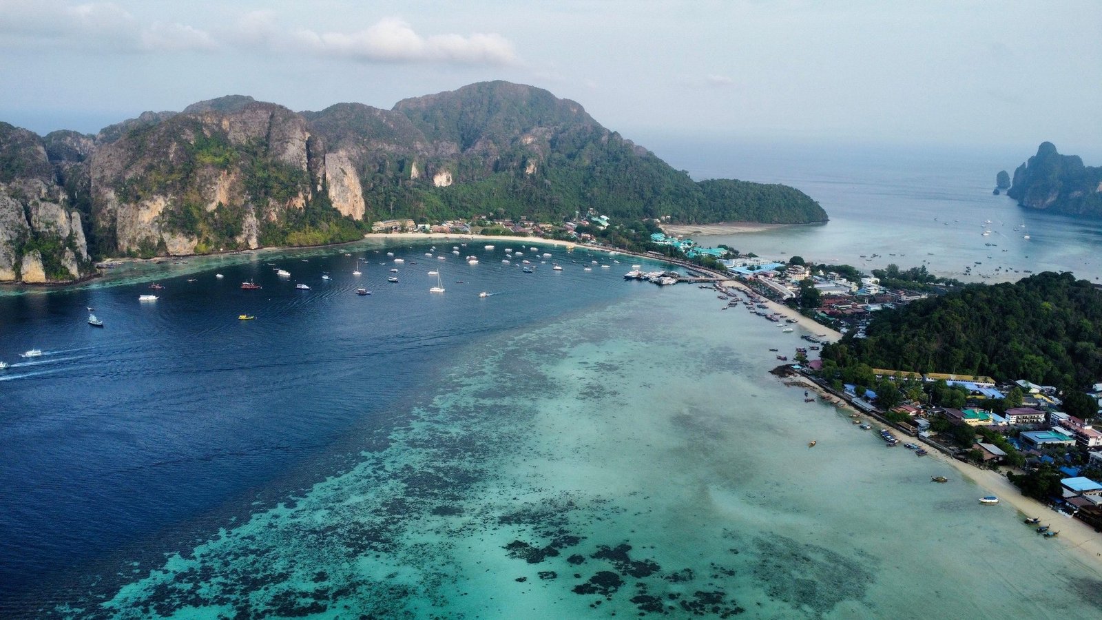 Phi Phi Don from the air, the village strung along the sand below the cliffs and a reef in the shallows
