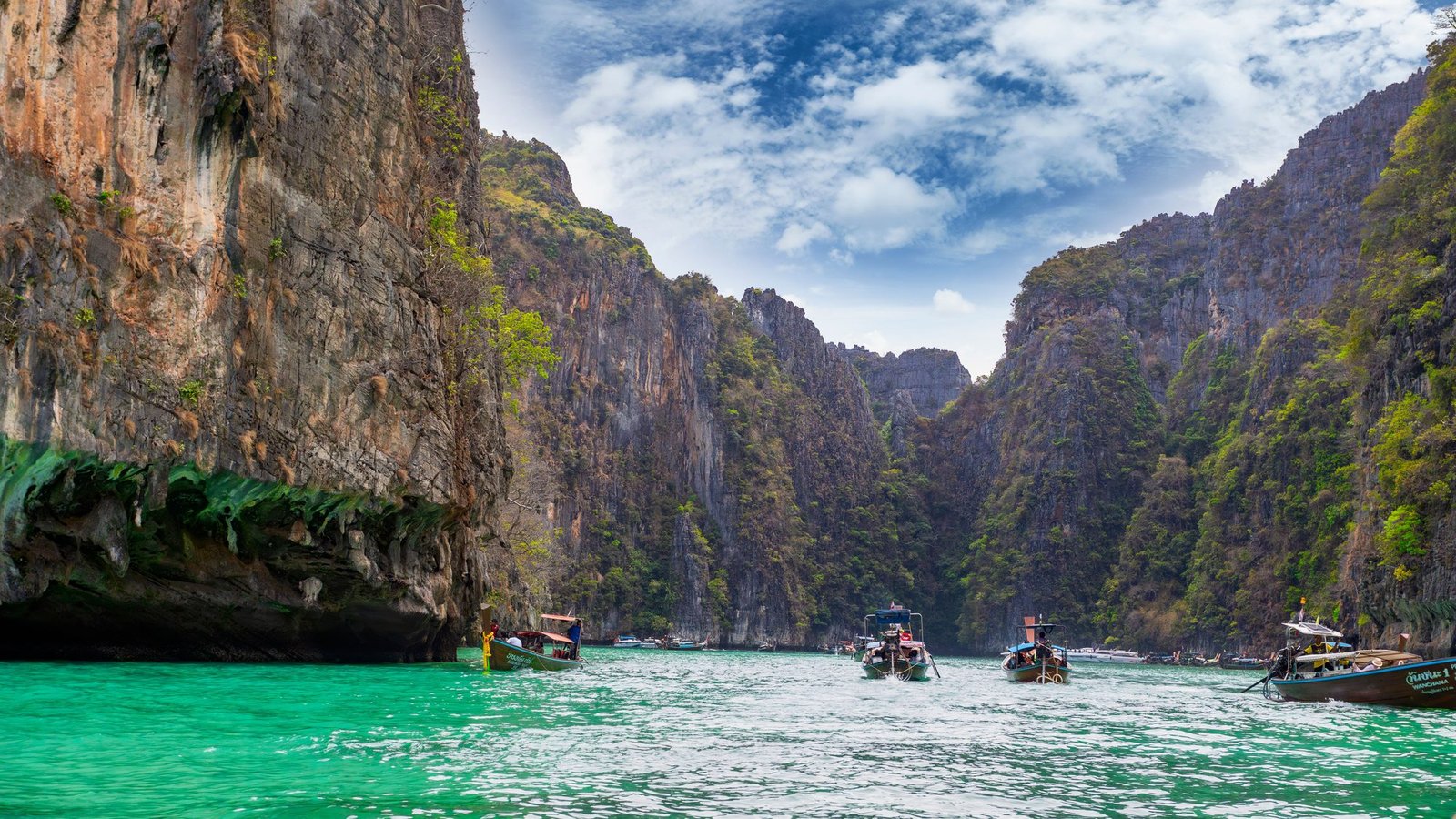 Longtail boats entering an emerald channel between sheer limestone walls