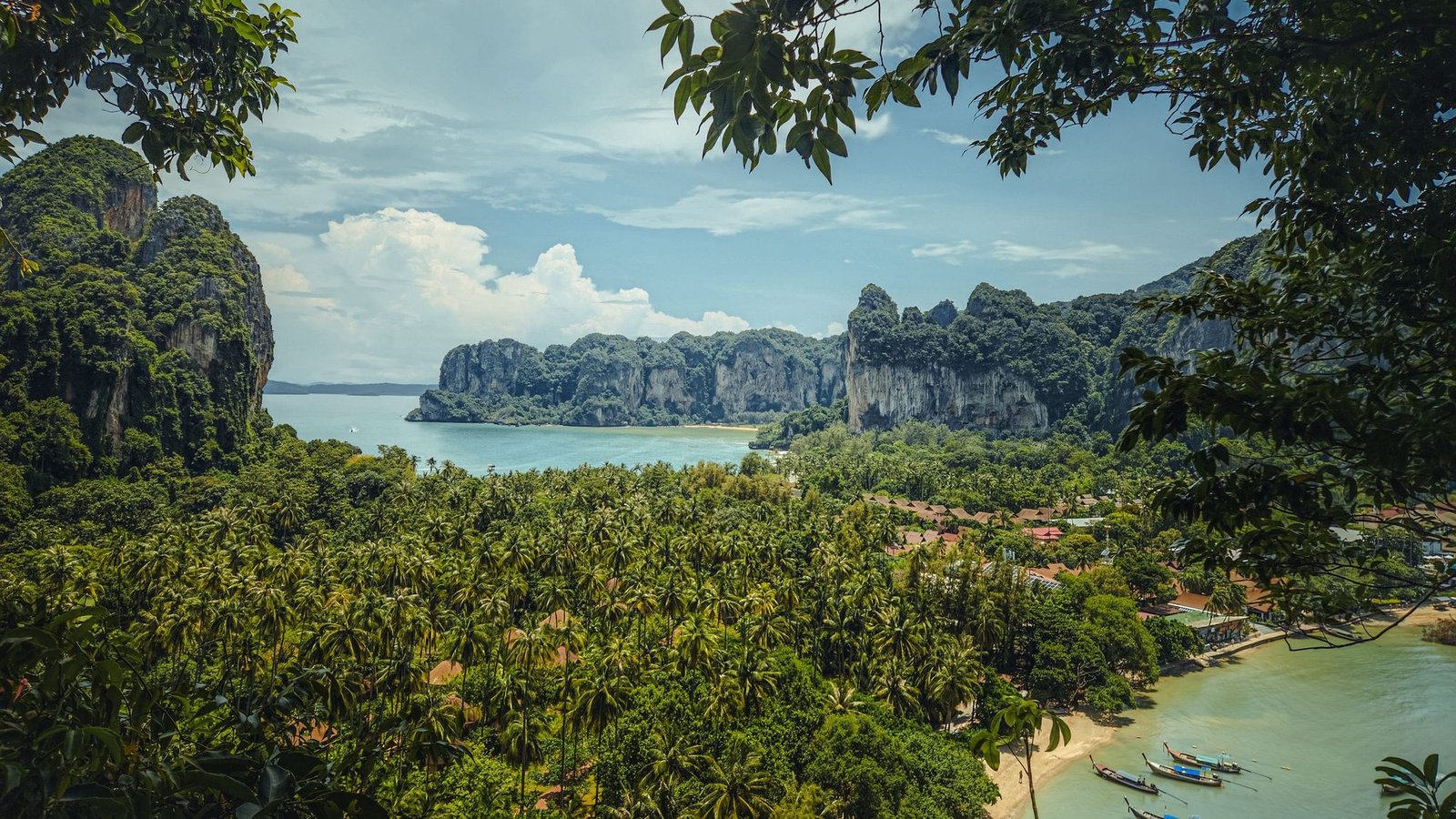 A palm-covered peninsula between limestone cliffs, seen from a viewpoint through the trees, in Krabi province