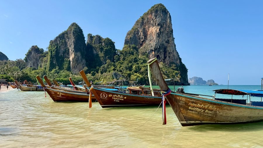 Longtail boats in shallow water at Railay West, below the limestone towers at the south end of the beach