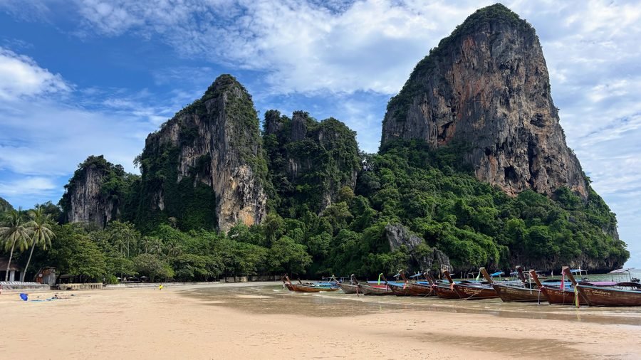 Longtail boats lined up at low tide on Railay Beach beneath towering limestone cliffs