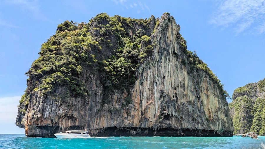 A speedboat at the foot of a sheer limestone cliff in turquoise water