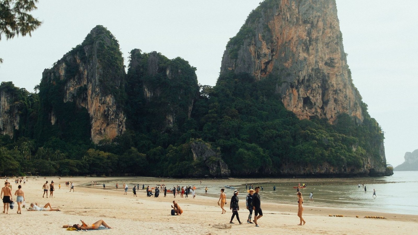 Une plage de sable sous un haut piton calcaire, avec des baigneurs sur le sable