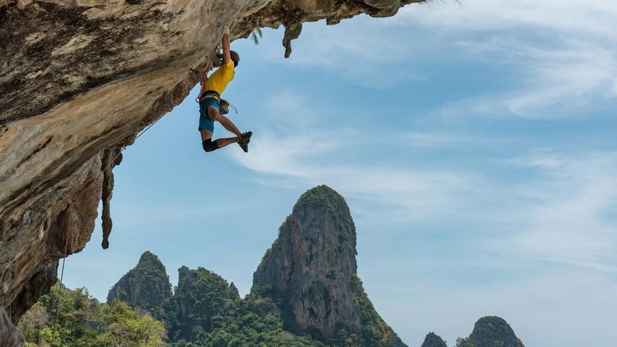 Un grimpeur sous un surplomb calcaire à Tonsai, falaises de Railay et mer en fond